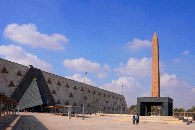 Exterior View of the Grand Egyptian Museum with its modern architecture , wide plaza and the tall Ramses II obelisk.