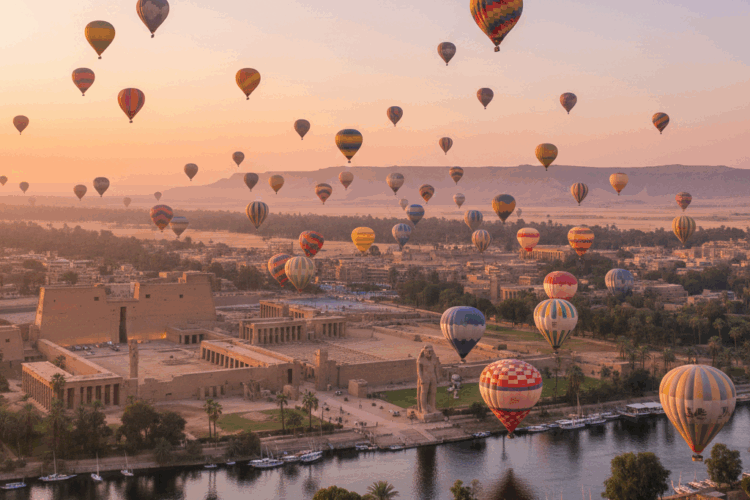Hot air balloons flying over Luxor at sunrise, overlooking ancient temples along the Nile River and the West Bank of Egypt